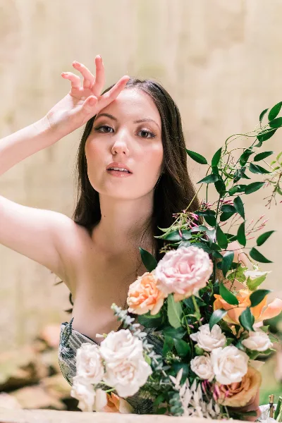 Close-up portrait of a woman with professional makeup and styled hair holding a bouquet of flowers.