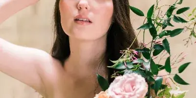 Close-up portrait of a woman with professional makeup and styled hair holding a bouquet of flowers.