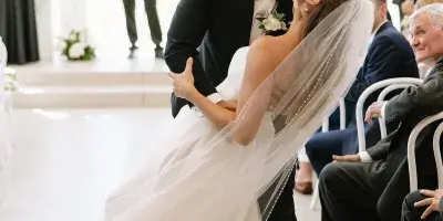 A bride and groom share a kiss during their wedding ceremony in a bright, modern venue with guests seated in the background.