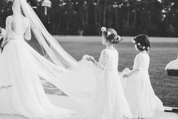 A black and white photograph of a bride and two flower girls in an outdoor setting.