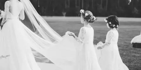A black and white photograph of a bride and two flower girls in an outdoor setting.