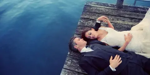 A bride and groom lying on a wooden dock next to a body of water.