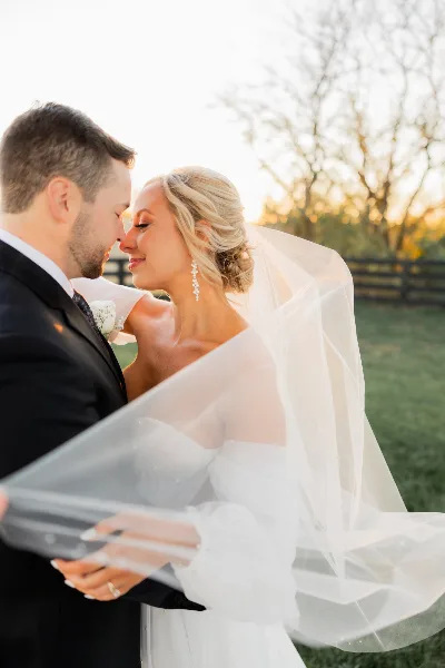 A bride and groom share an intimate moment outdoors, with the bride's veil blowing in the wind.
