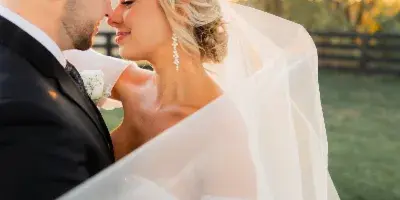 A bride and groom share an intimate moment outdoors, with the bride's veil blowing in the wind.