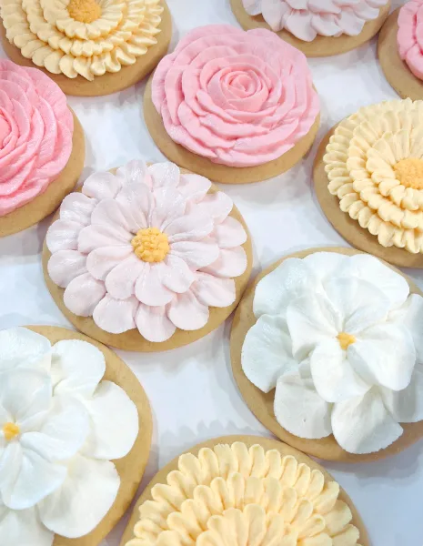 Close-up of decorated sugar cookies featuring intricate buttercream flower designs in pink, white, and yellow.