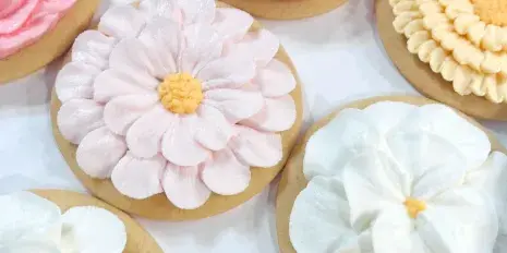 Close-up of decorated sugar cookies featuring intricate buttercream flower designs in pink, white, and yellow.