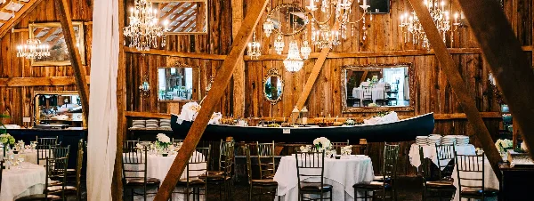 Interior of a rustic wooden barn wedding venue featuring chandeliers, mirrors, and set dining tables with white linens.