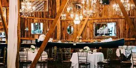 Interior of a rustic wooden barn wedding venue featuring chandeliers, mirrors, and set dining tables with white linens.