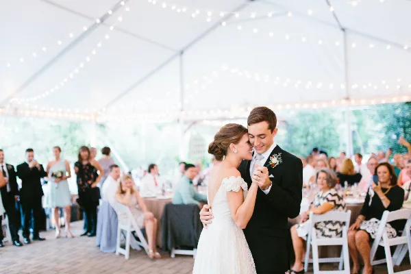 A bride and groom dancing at a wedding reception under a white tent with string lights.