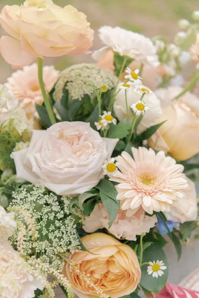 Close-up of a wedding floral arrangement featuring blush and cream roses, daisies, and greenery.