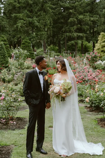 A bride and groom standing together in a rose garden, with the bride holding a bouquet.