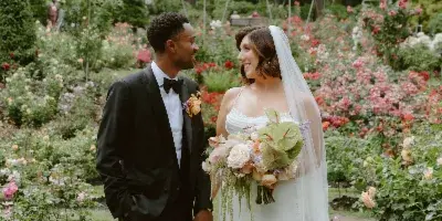 A bride and groom standing together in a rose garden, with the bride holding a bouquet.