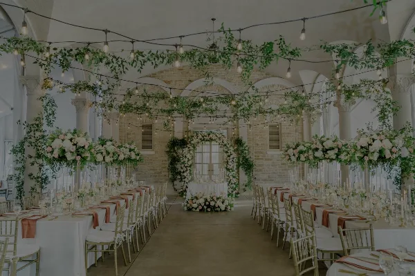 Wedding reception hall decorated with overhead floral garlands, a floral arch, and large floral centerpieces on tables.