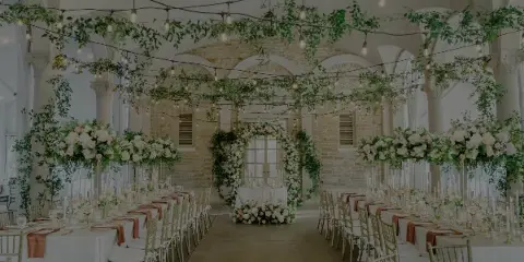 Wedding reception hall decorated with overhead floral garlands, a floral arch, and large floral centerpieces on tables.