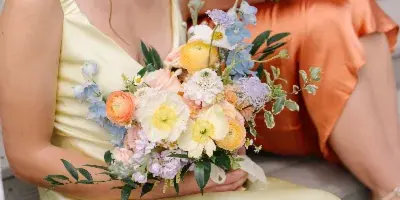 A bride and bridesmaid holding colorful wedding bouquets featuring roses, ranunculus, and delphinium.