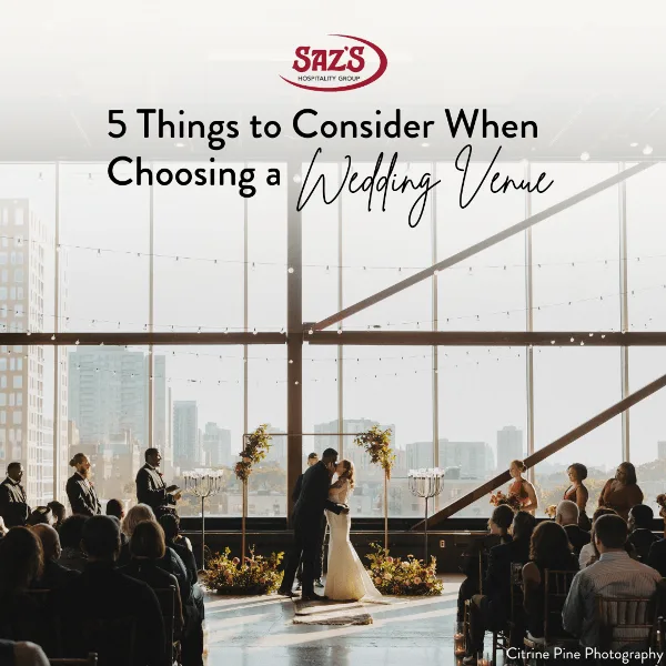 A wedding couple sharing a first kiss during a ceremony in a bright, modern event space with large windows overlooking a city skyline.