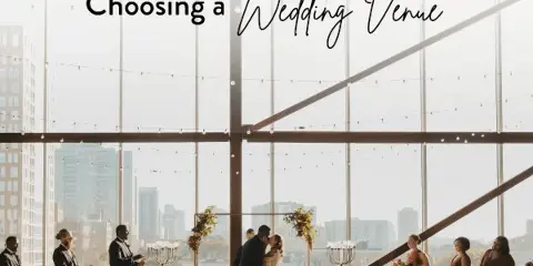 A wedding couple sharing a first kiss during a ceremony in a bright, modern event space with large windows overlooking a city skyline.