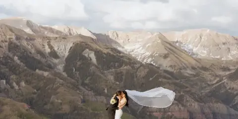 A bride and groom kissing on a wooden platform with a mountain range in the background.