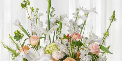 A large, elegant floral arrangement featuring white lilies, roses, and greenery on a silver tray.
