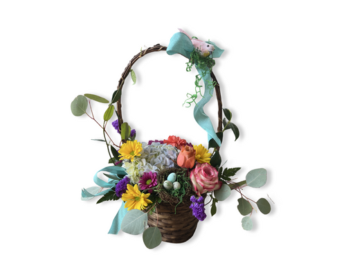 A floral arrangement featuring yellow, pink, and purple flowers in a woven basket with a decorative ribbon.