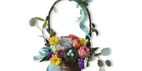 A floral arrangement featuring yellow, pink, and purple flowers in a woven basket with a decorative ribbon.