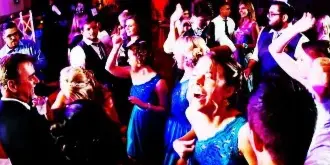A crowded dance floor at a wedding reception with guests dancing under blue and purple lighting.