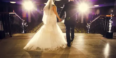 A bride and groom walking down a staircase in a ballroom, viewed from behind.