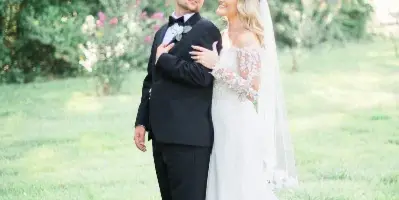 A bride and groom standing together in a grassy field with trees in the background.