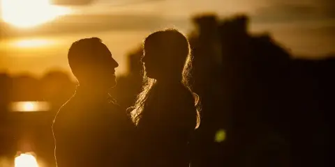 A romantic silhouette of a couple facing each other against a golden sunset.