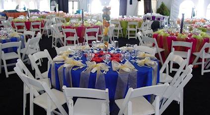 A large event space set up with numerous round tables covered in colorful linens and surrounded by white chairs.