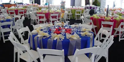 A large event space set up with numerous round tables covered in colorful linens and surrounded by white chairs.