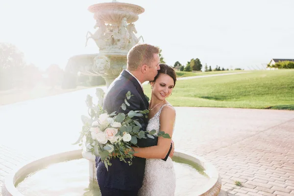 A bride and groom embracing in front of a stone fountain during a wedding.