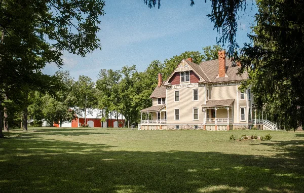 Exterior view of a historic Queen Anne mansion and a red barn on a grassy estate lawn.