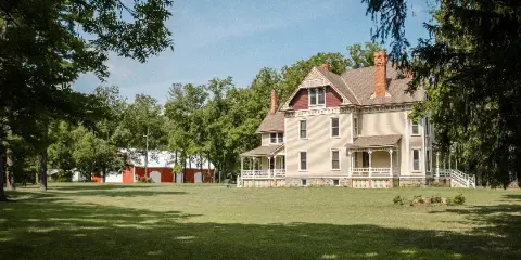 Exterior view of a historic Queen Anne mansion and a red barn on a grassy estate lawn.