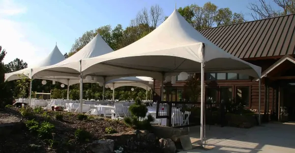 A large white marquee tent set up outdoors with tables and chairs, adjacent to a building.