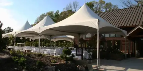 A large white marquee tent set up outdoors with tables and chairs, adjacent to a building.