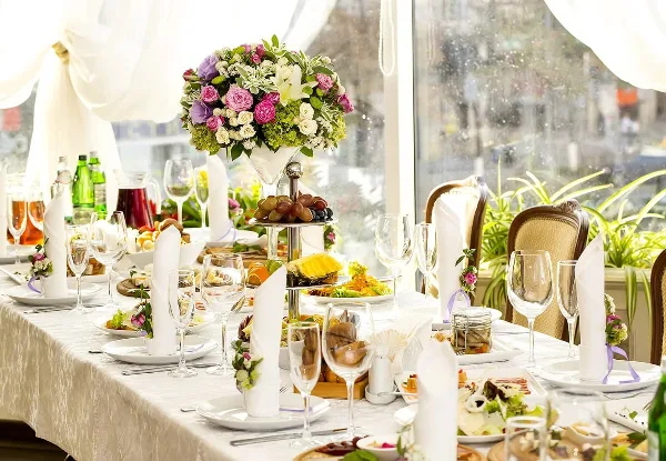 A formal event table setting featuring a floral centerpiece, glassware, and a tiered display of food.