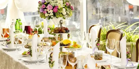 A formal event table setting featuring a floral centerpiece, glassware, and a tiered display of food.