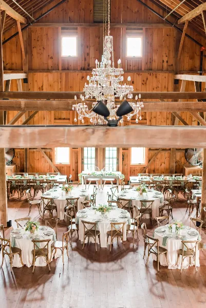 A rustic wooden event hall featuring multiple round tables set with white table linens, china, and glassware, ready for a wedding or event.