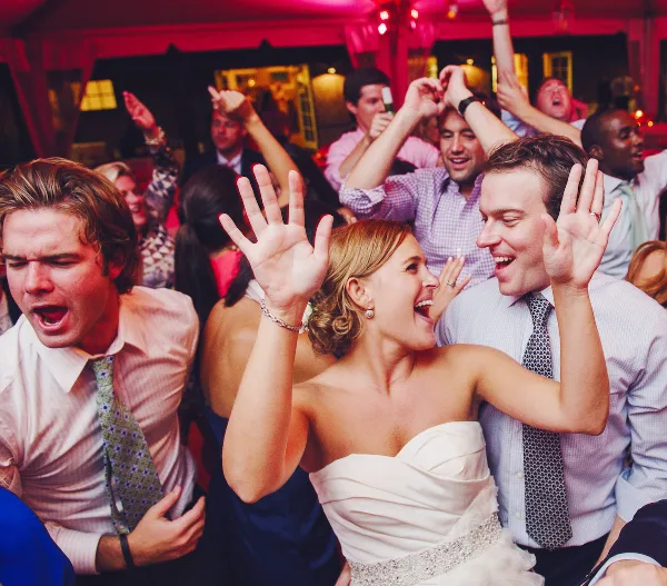A bride and wedding guests dancing and celebrating at a reception.