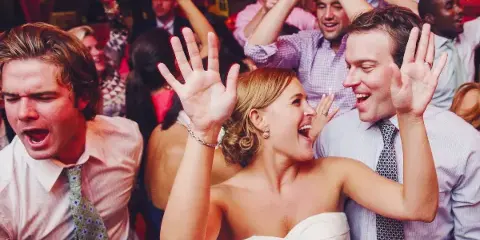 A bride and wedding guests dancing and celebrating at a reception.