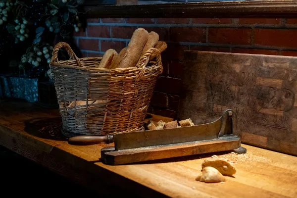 A wicker basket filled with baguettes and a wooden sign for The Vineyard Restaurant & Bar sitting on a wooden counter.