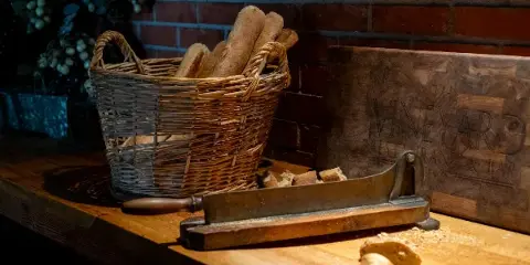 A wicker basket filled with baguettes and a wooden sign for The Vineyard Restaurant & Bar sitting on a wooden counter.