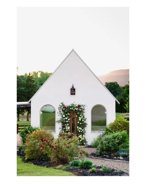 Exterior view of a white stucco wedding chapel with arched windows and a floral doorway, set against a mountain landscape.