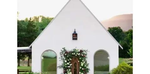Exterior view of a white stucco wedding chapel with arched windows and a floral doorway, set against a mountain landscape.