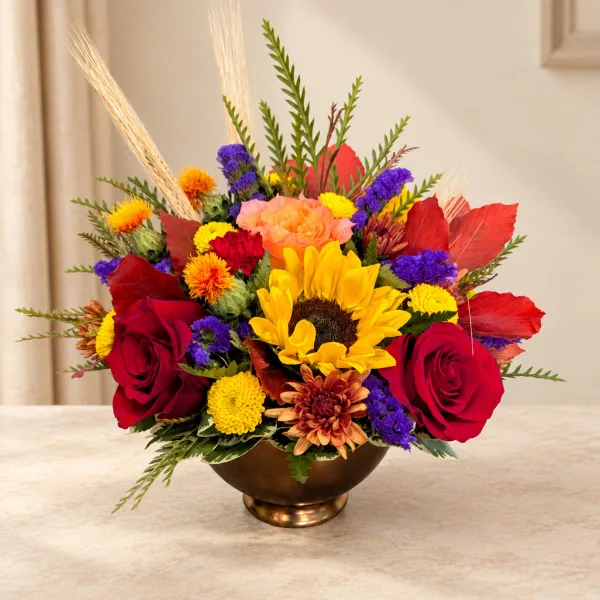 A mixed floral arrangement with sunflowers, red roses, and colorful mums in a bronze bowl vase.