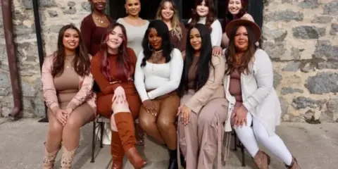 A group of ten women, presumably the beauty team, posing together in front of a stone building.