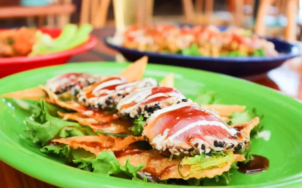 A close-up of a plated appetizer featuring tuna and wonton strips on a green plate in a restaurant setting.