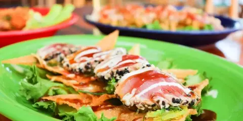 A close-up of a plated appetizer featuring tuna and wonton strips on a green plate in a restaurant setting.