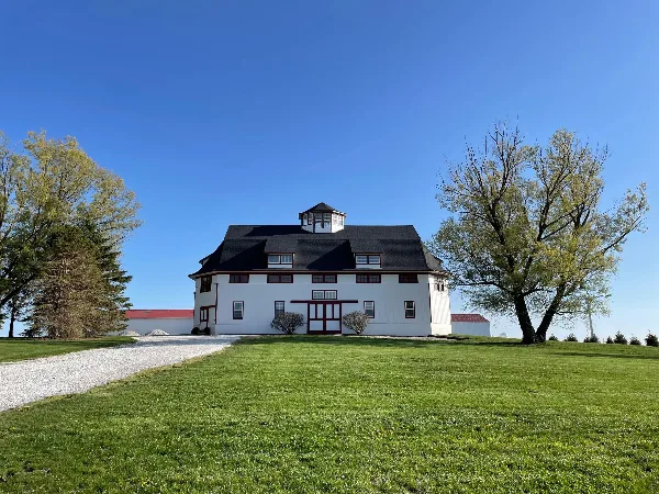 Exterior view of a white historic barn wedding venue with a dark roof and cupola on a grassy lawn under a blue sky.
